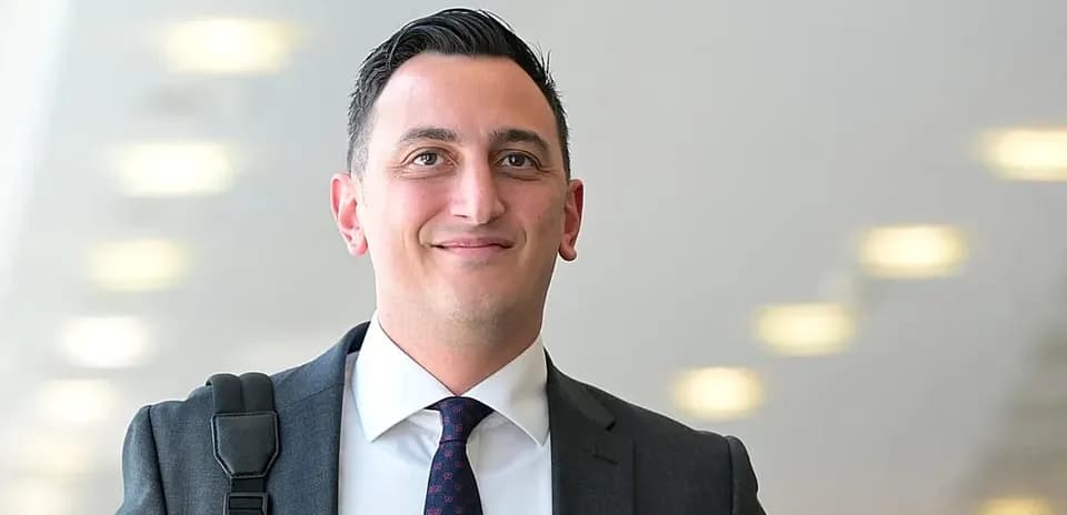 Man in suit smiling with bag over shoulder