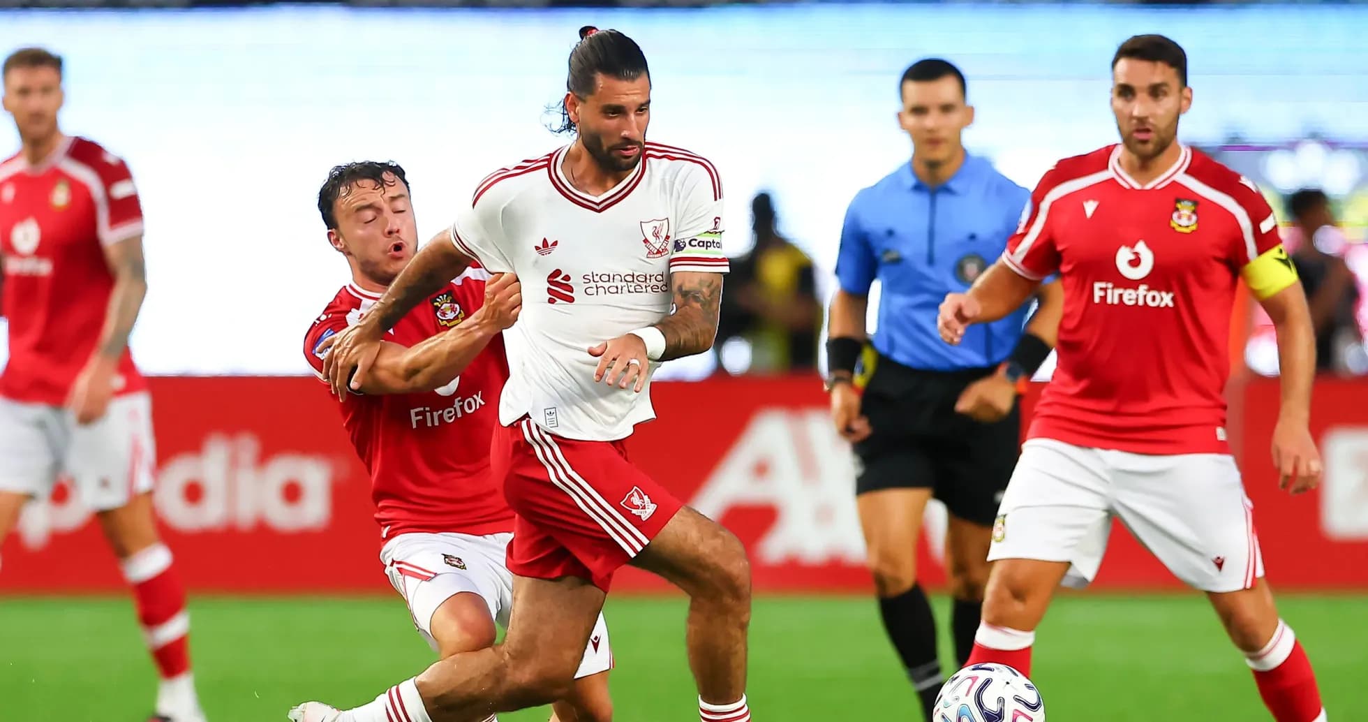 Futbolchilar to'p uchun kurashmoqda, orqa fonda hakam