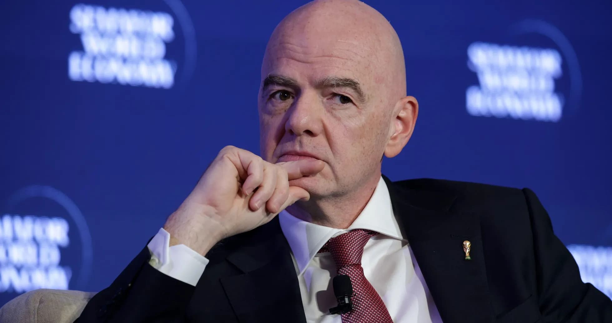 Man speaking at a conference with a thoughtful expression