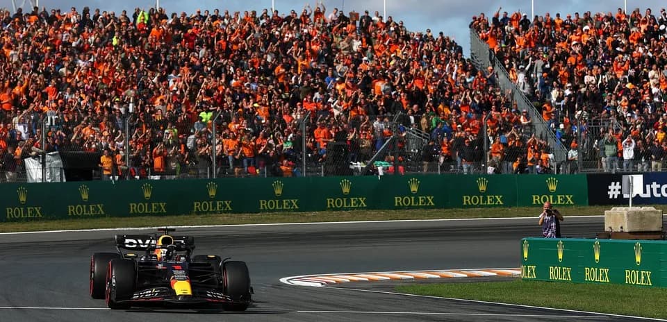 Formula 1 car racing past cheering crowd in orange