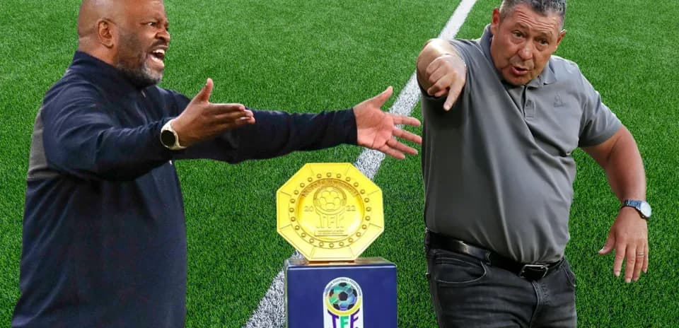 Two football coaches gesturing beside trophy on pitch