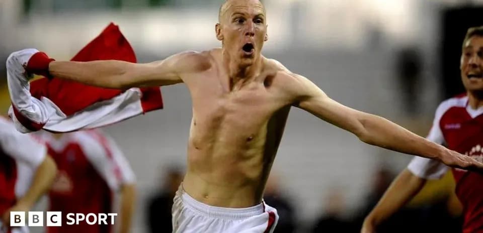 Player celebrating goal with shirt raised in stadium