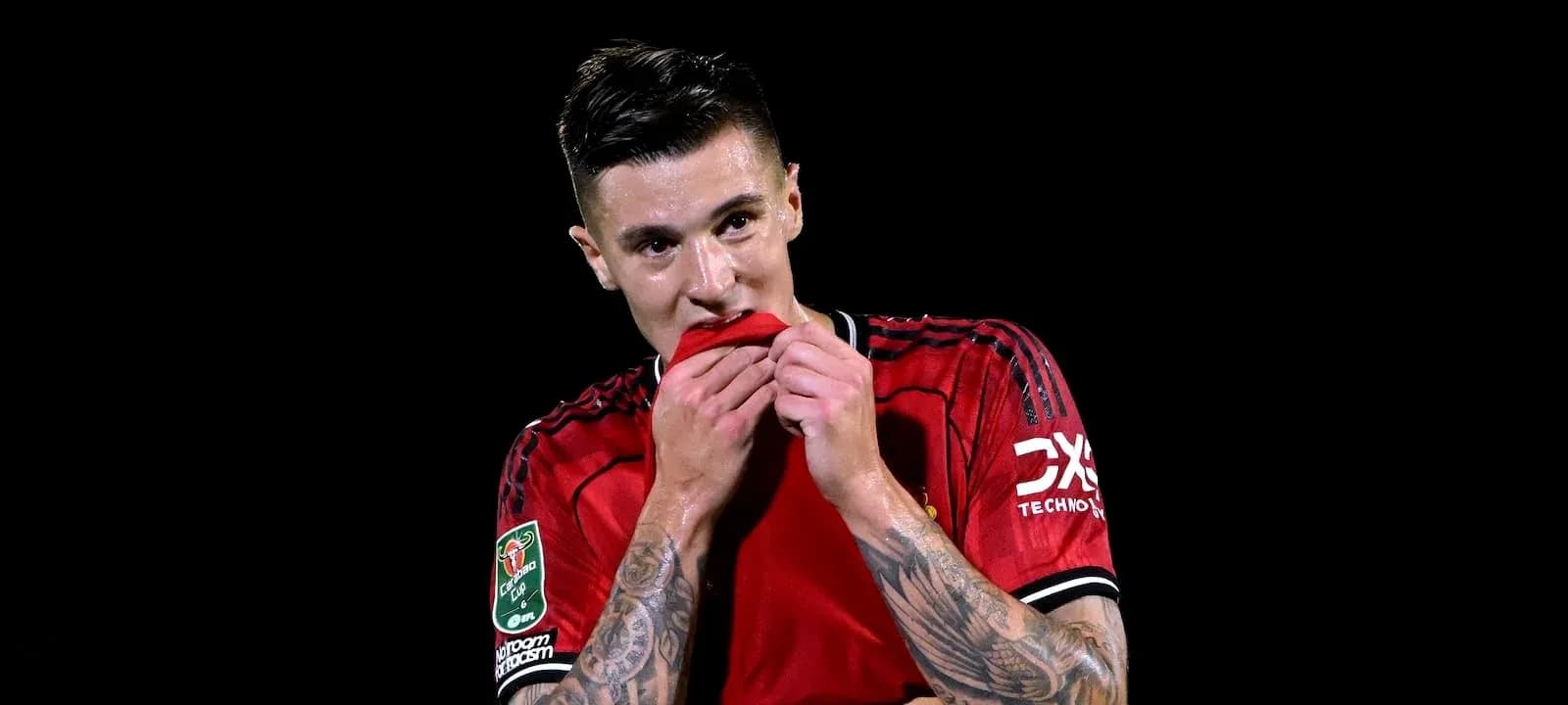 Futbolchi qizil forma kiyib, ko'ylagini tishlayapti