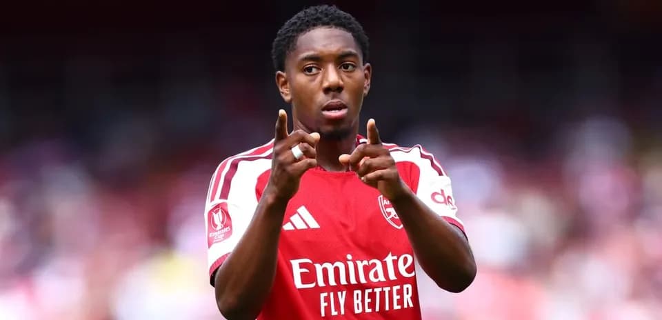 Futbolchi Arsenal formasida maydonda ishora qilmoqda