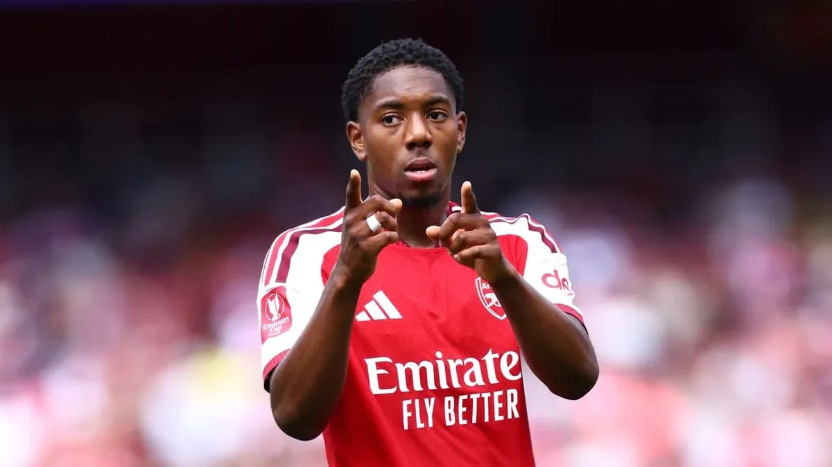 Futbolchi Arsenal formasida maydonda ishora qilmoqda