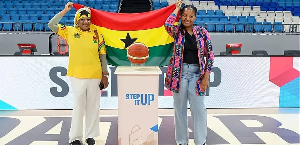 Two women holding Ghana flag and basketball on court