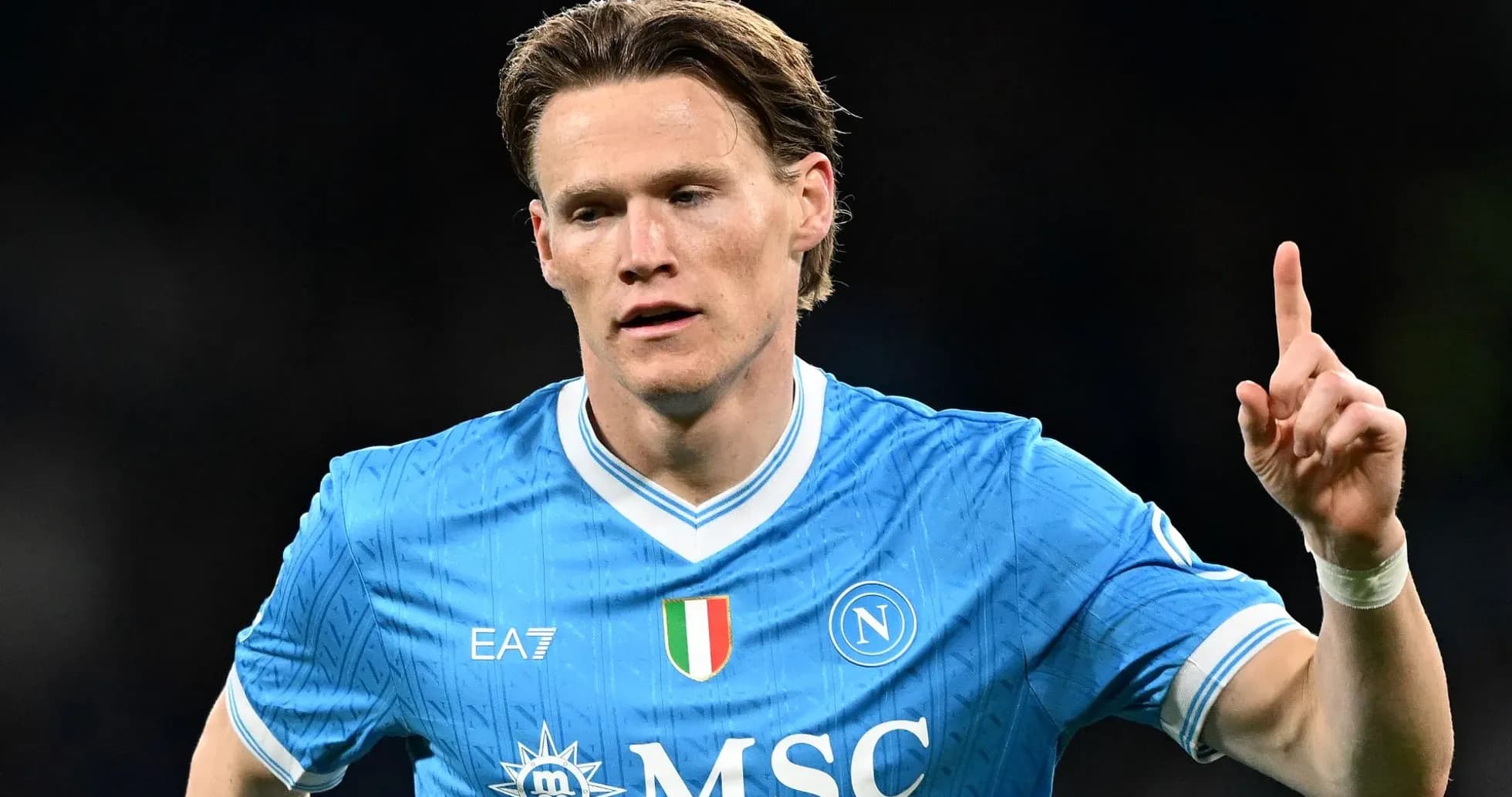 Futbolchi Napoli formasida, bir qo'lni ko'tarib turibdi