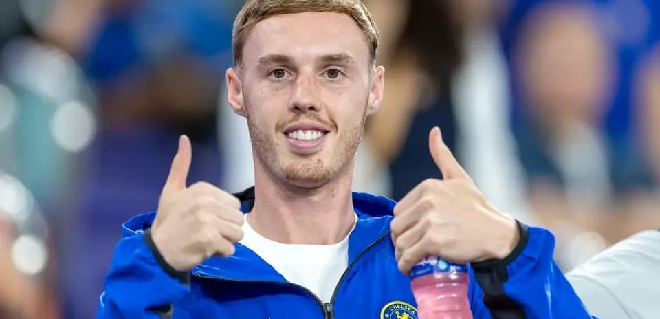 Futbolchi Chelsea futbolka kiygan, ikki barmoqni ko'tarib turibdi