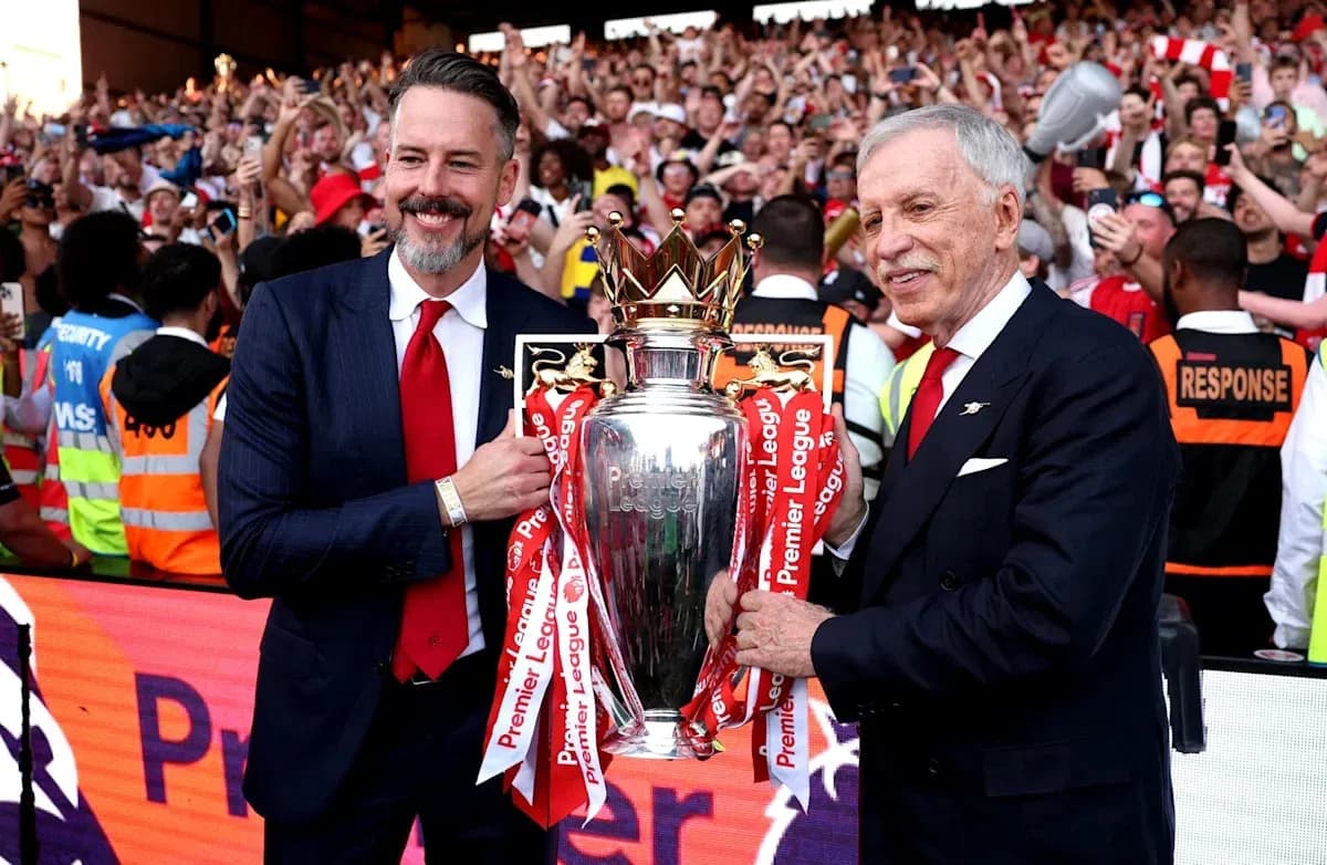 Two officials holding Premier League trophy with fans celebrating