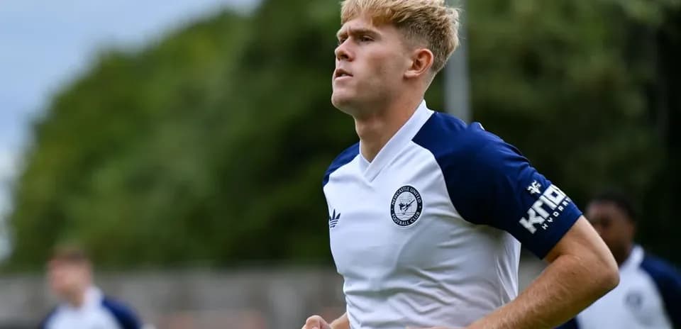 Futbolchi mashg'ulotda yugurmoqda, orqada boshqa o'yinchilar