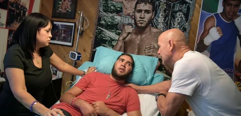 Young man in hospital bed with two visitors