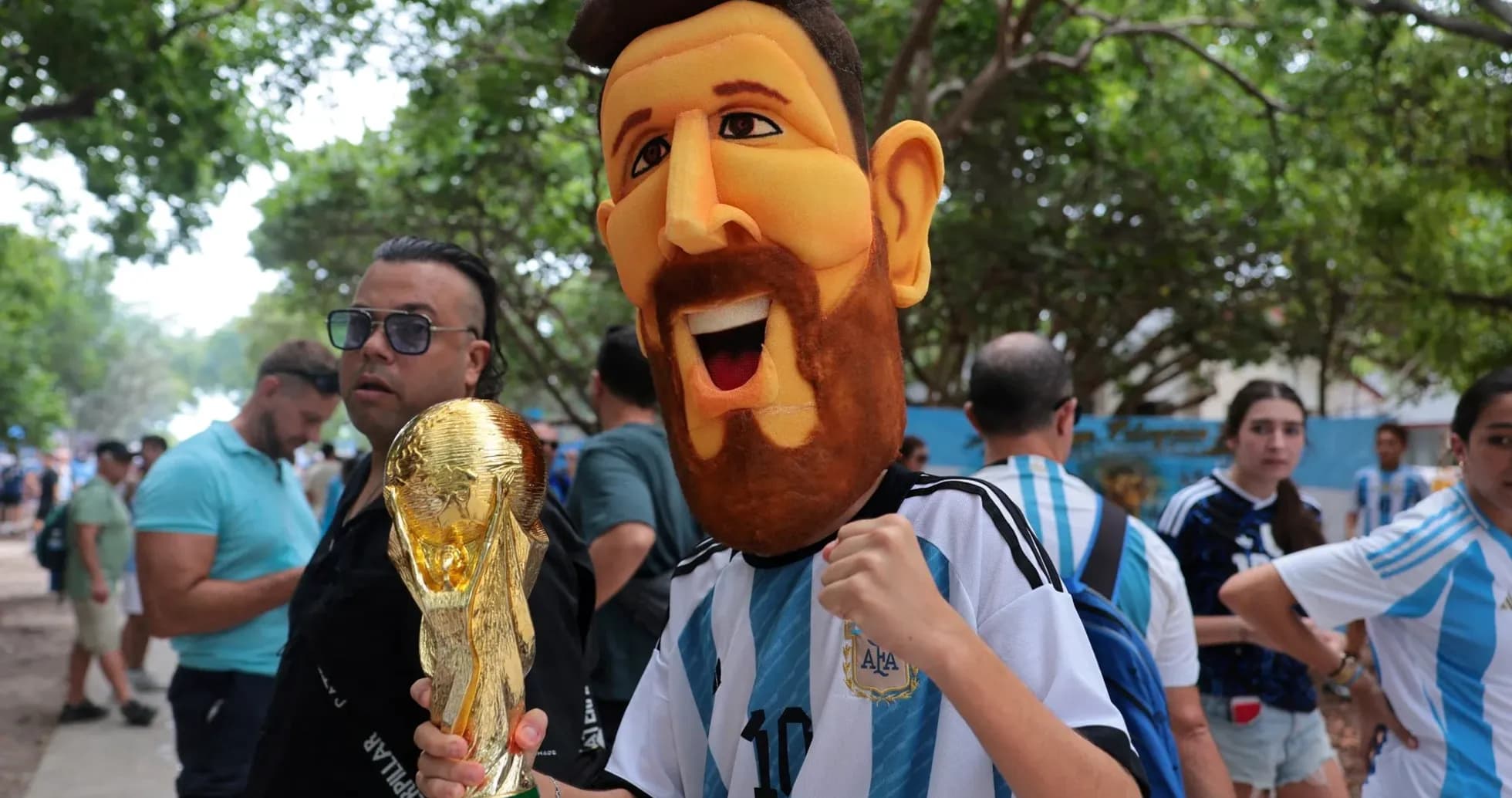 Fan wearing Messi mask holding World Cup trophy
