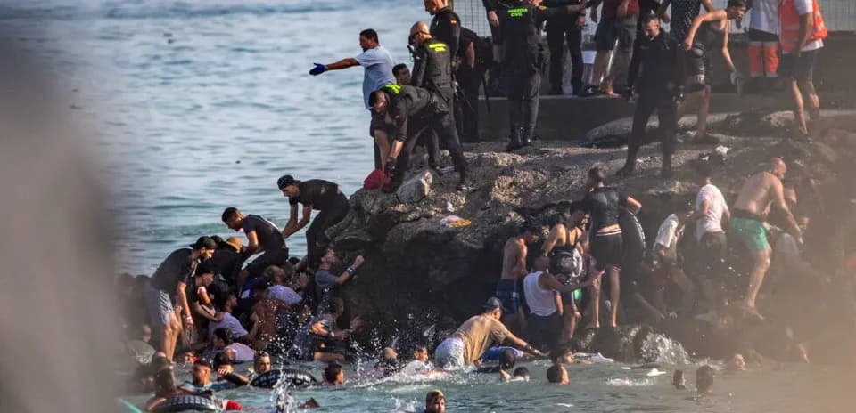 People in water near rocky shore with authorities present
