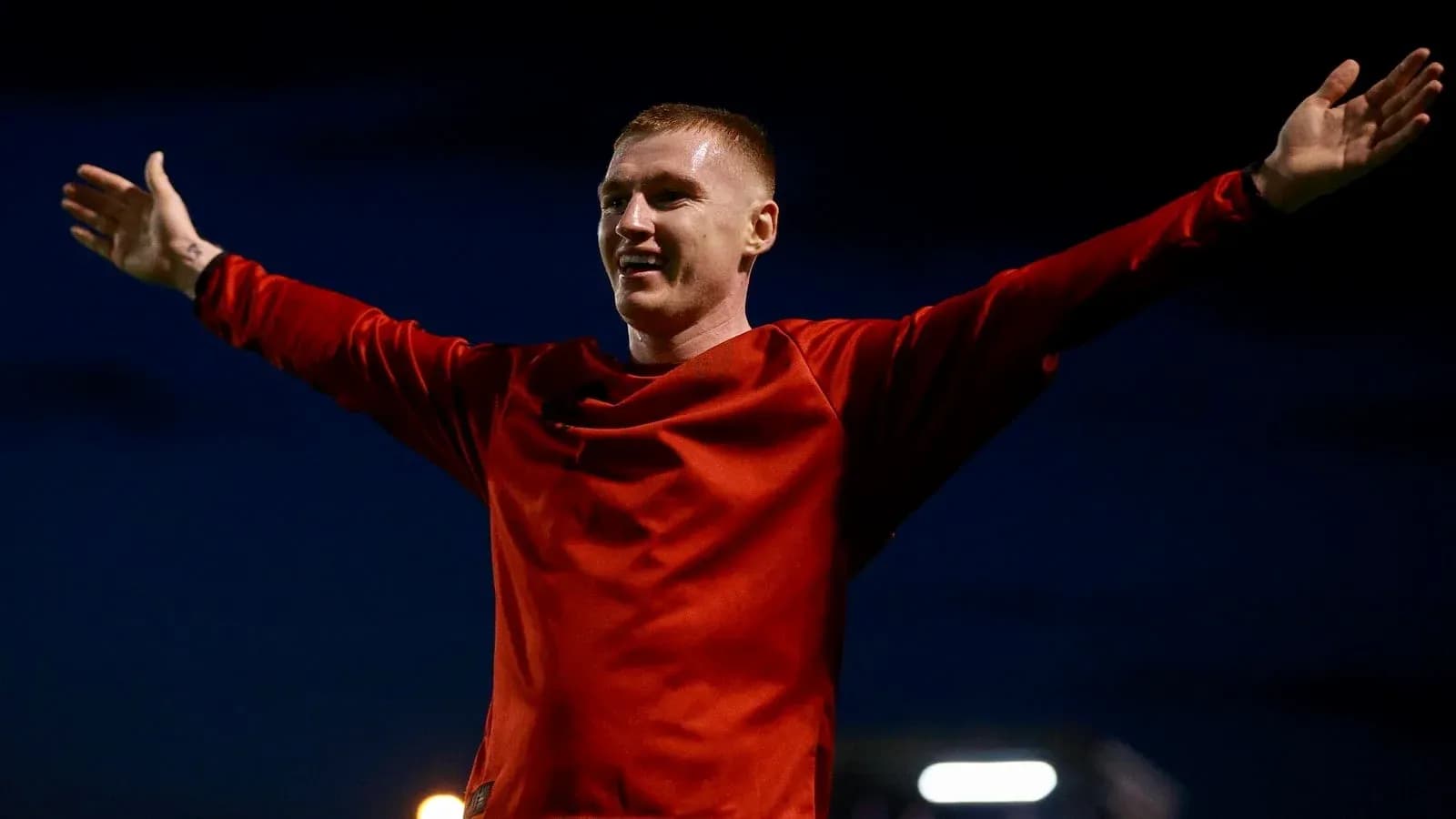 Futbolchi qizil formada qo'llarini keng yoygan