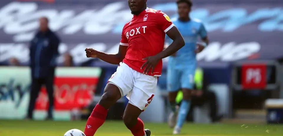 Futbolchi qizil futbolka kiyib, to'pni haydayapti