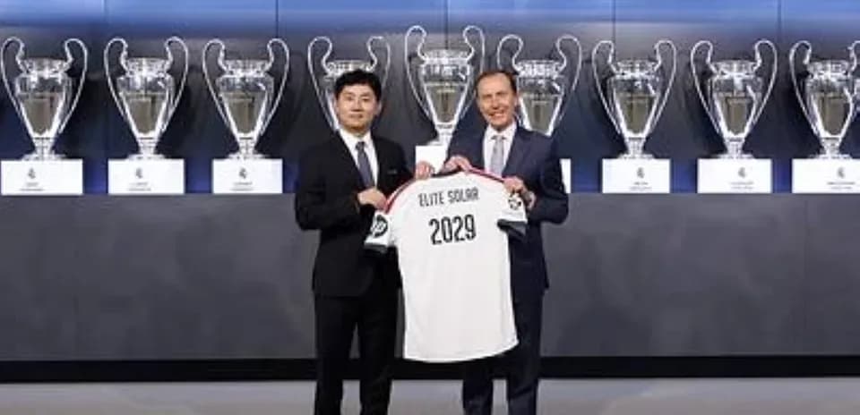 Two men holding jersey in front of trophies