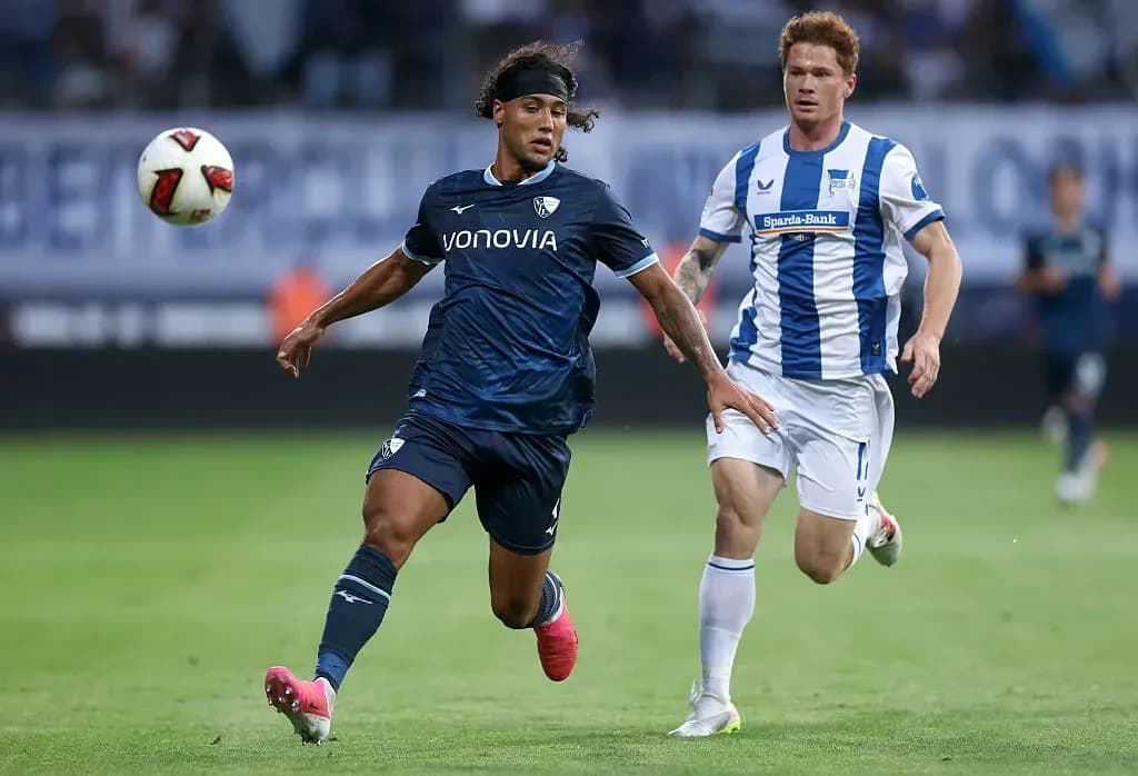 Player in dark kit chasing ball with opponent behind