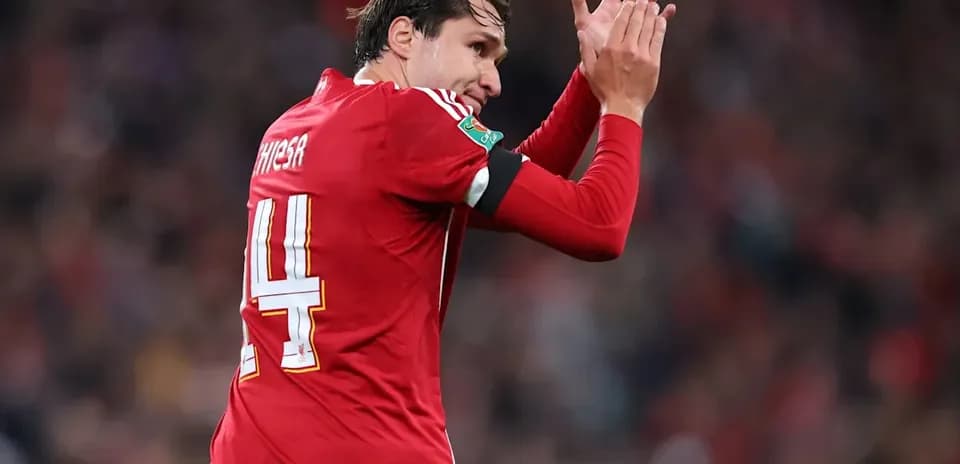 Futbolchi maydonda qizil formada qo'l silkitmoqda