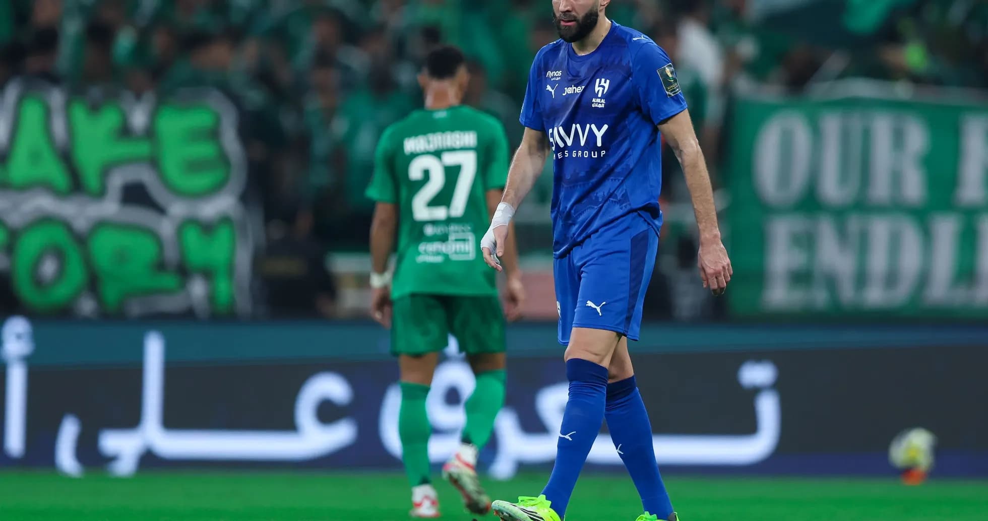Futbolchilar maydonda harakat qilmoqda, tomoshabinlar ko'rinadi