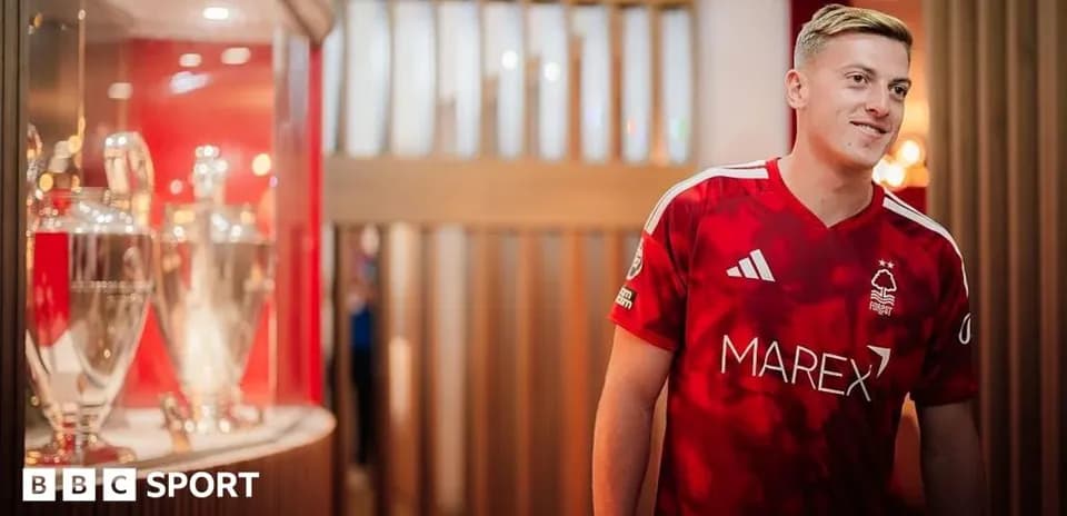 Futbolchi qizil forma kiygan, kuboklar oldida