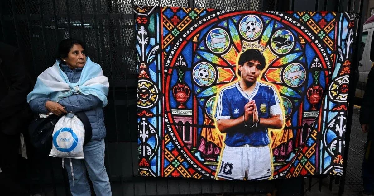 Ayol Argentina bayrog'ini o'rab olgan, devorda Diego Maradona rasmli plakat Ayol Argentina bayrog'ini o'rab olgan, devorda Diego Maradona rasmli plakat